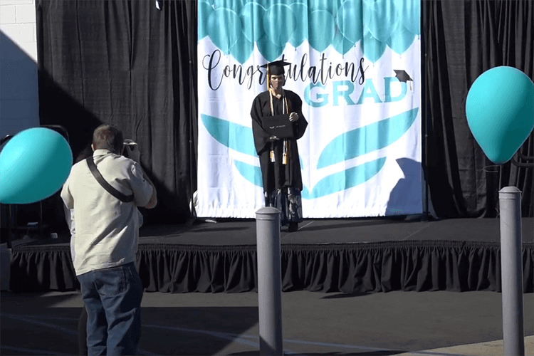 UEI College Oceanside Hosts Drive-Through Graduation - UEI UEI graduate on stage